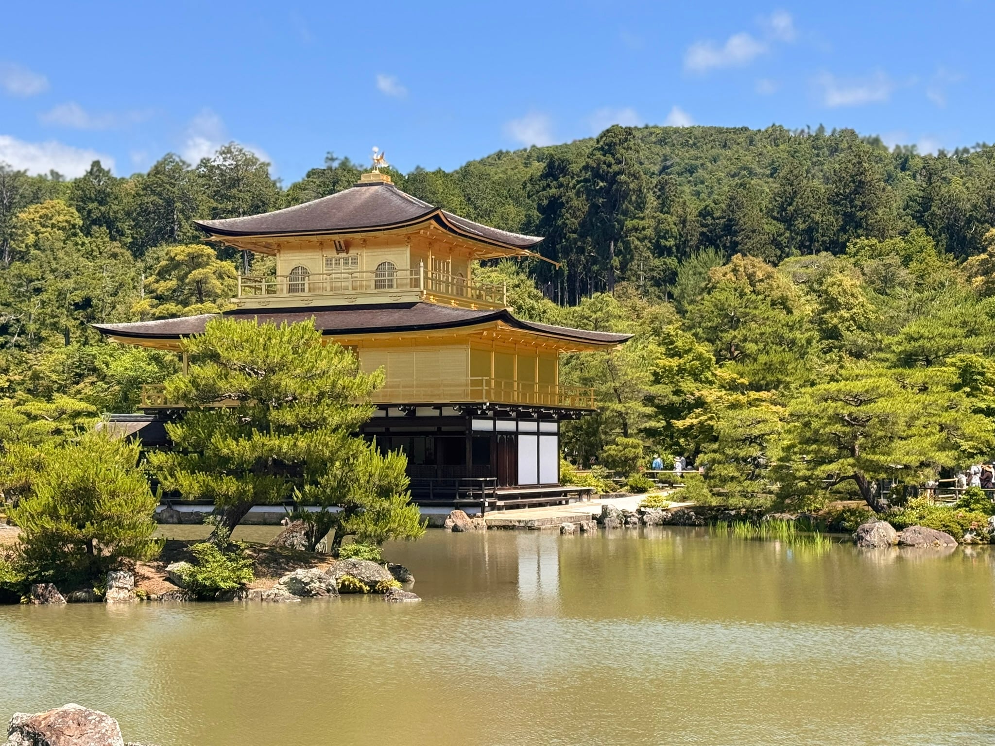 Kinkaku-ji, the golden pavilion, reflected in its pond under a bright blue Kyoto sky